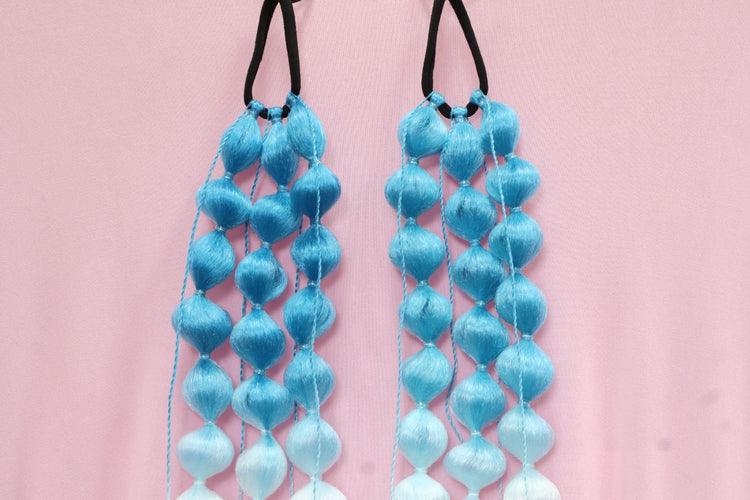 Pair of blue and white beaded hair ties on a pink background