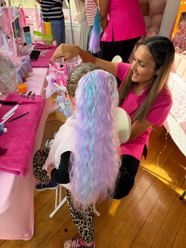 Stylist in pink fitting a long lilac and blue wavy hair extension at a birthday party