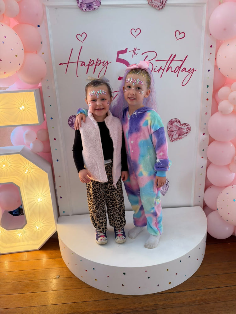 Two girls with face gems in front of the Happy 5th Birthday backdrop at Rose's party