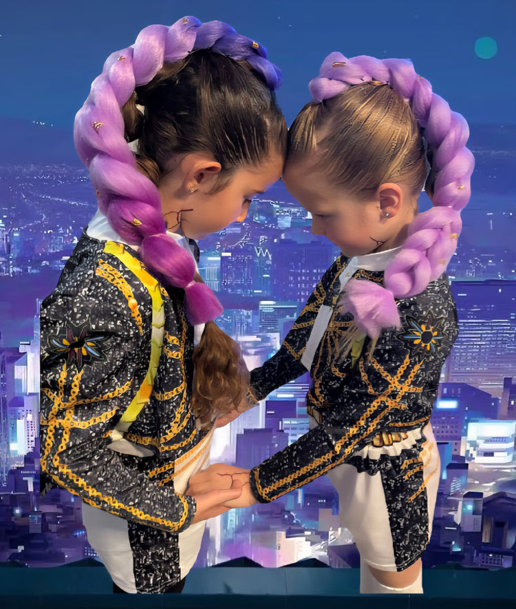Two children in matching outfits with pink braids against a cityscape background